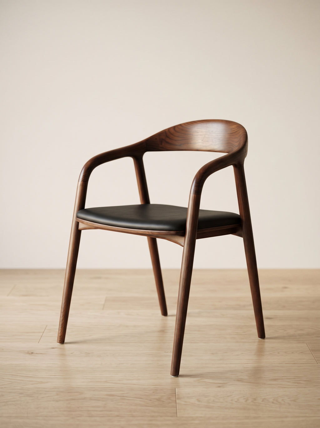 A mid-century modern wooden dining chair with a curved backrest, armrests, and a black upholstered seat, shown on a light wood floor against a neutral beige wall.