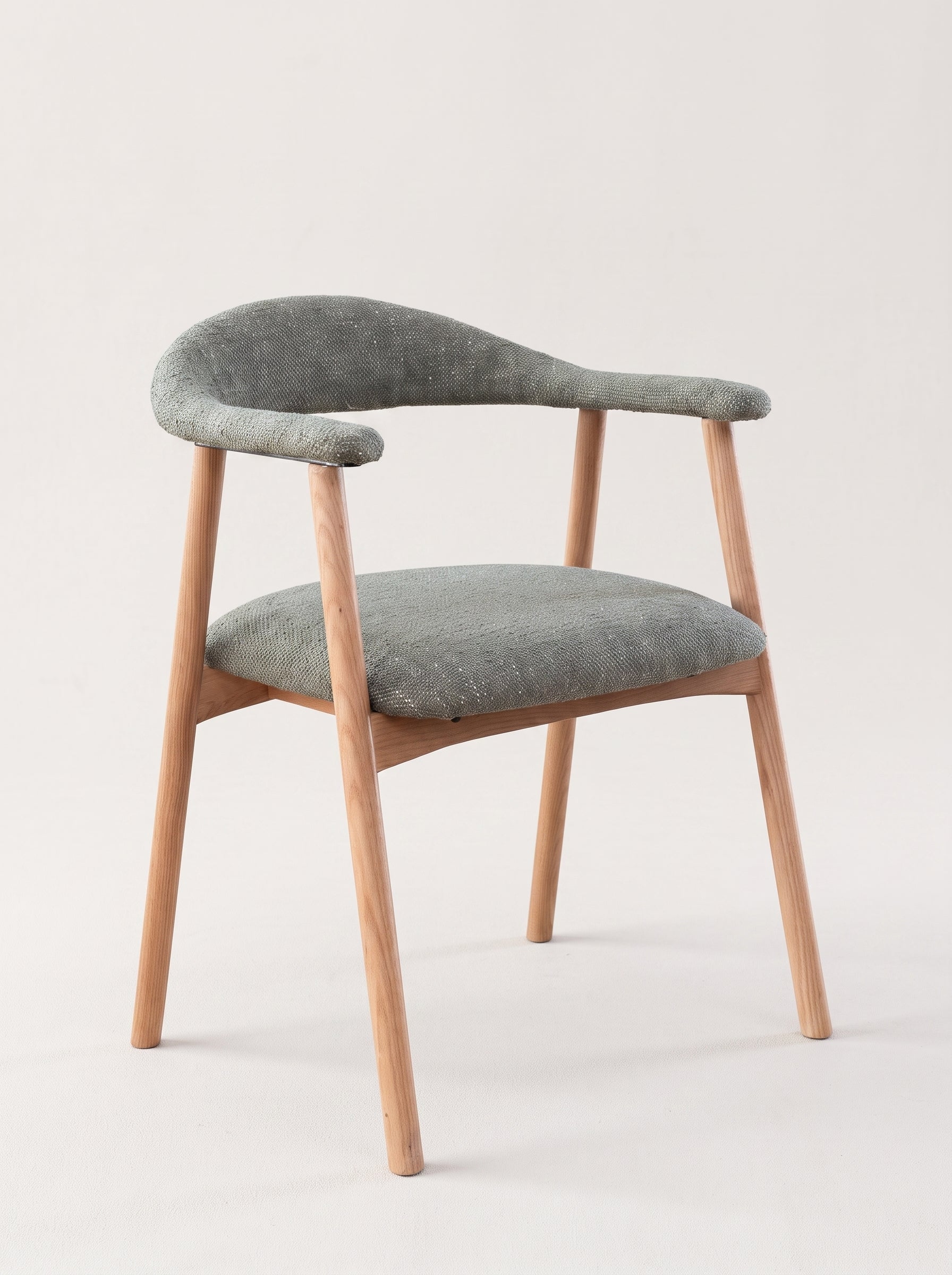 A modern armchair with a curved backrest and seat, upholstered in textured gray fabric with a natural light wood frame and tapered legs, shown against a plain off-white background.