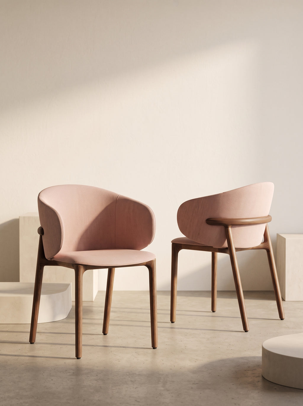 Two modern upholstered dining chairs with dusty pink curved seats and light brown wooden legs, set against a minimalist beige wall with soft diagonal shadows.