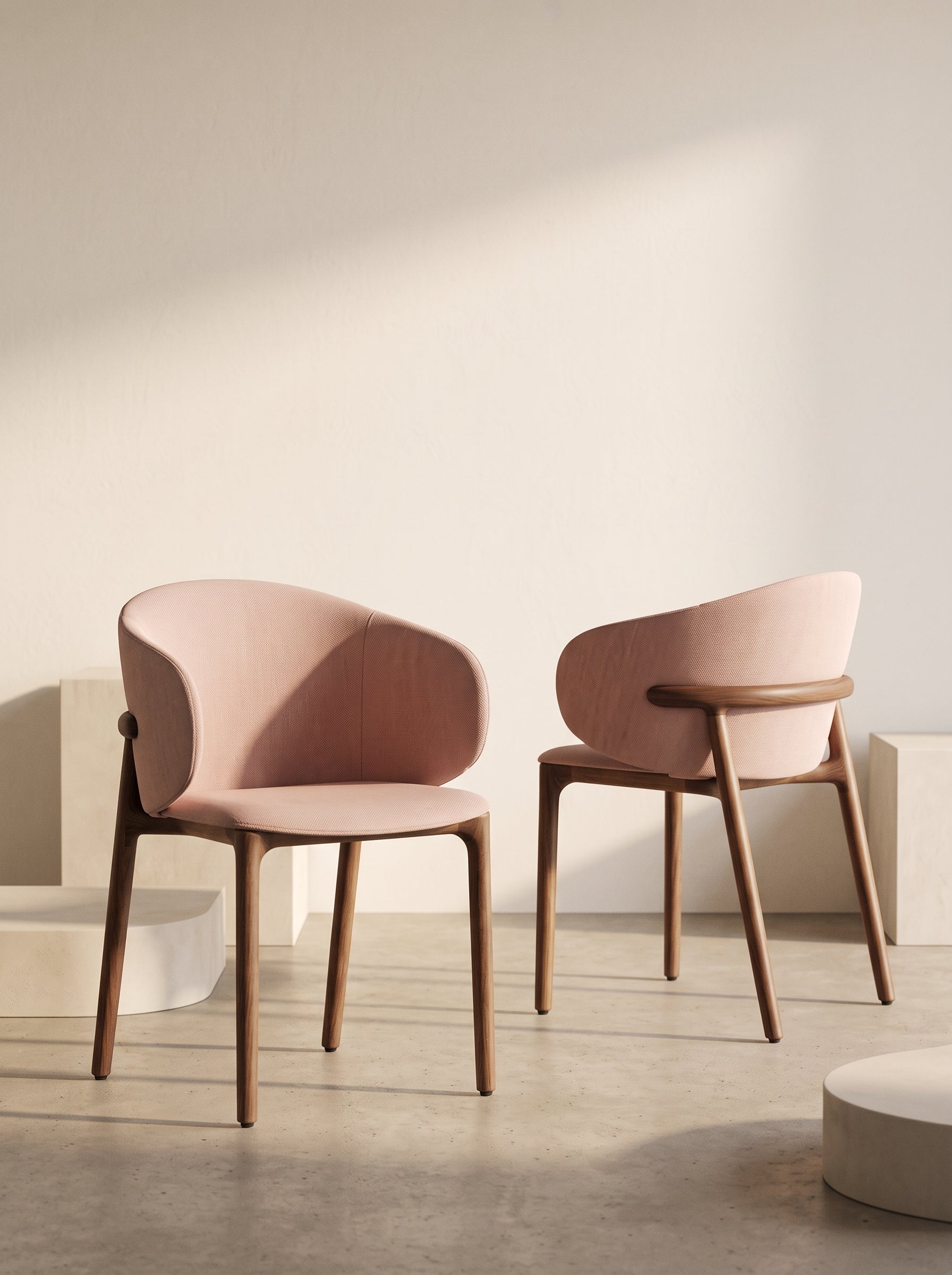 Two modern upholstered dining chairs with dusty pink curved seats and light brown wooden legs, set against a minimalist beige wall with soft diagonal shadows.
