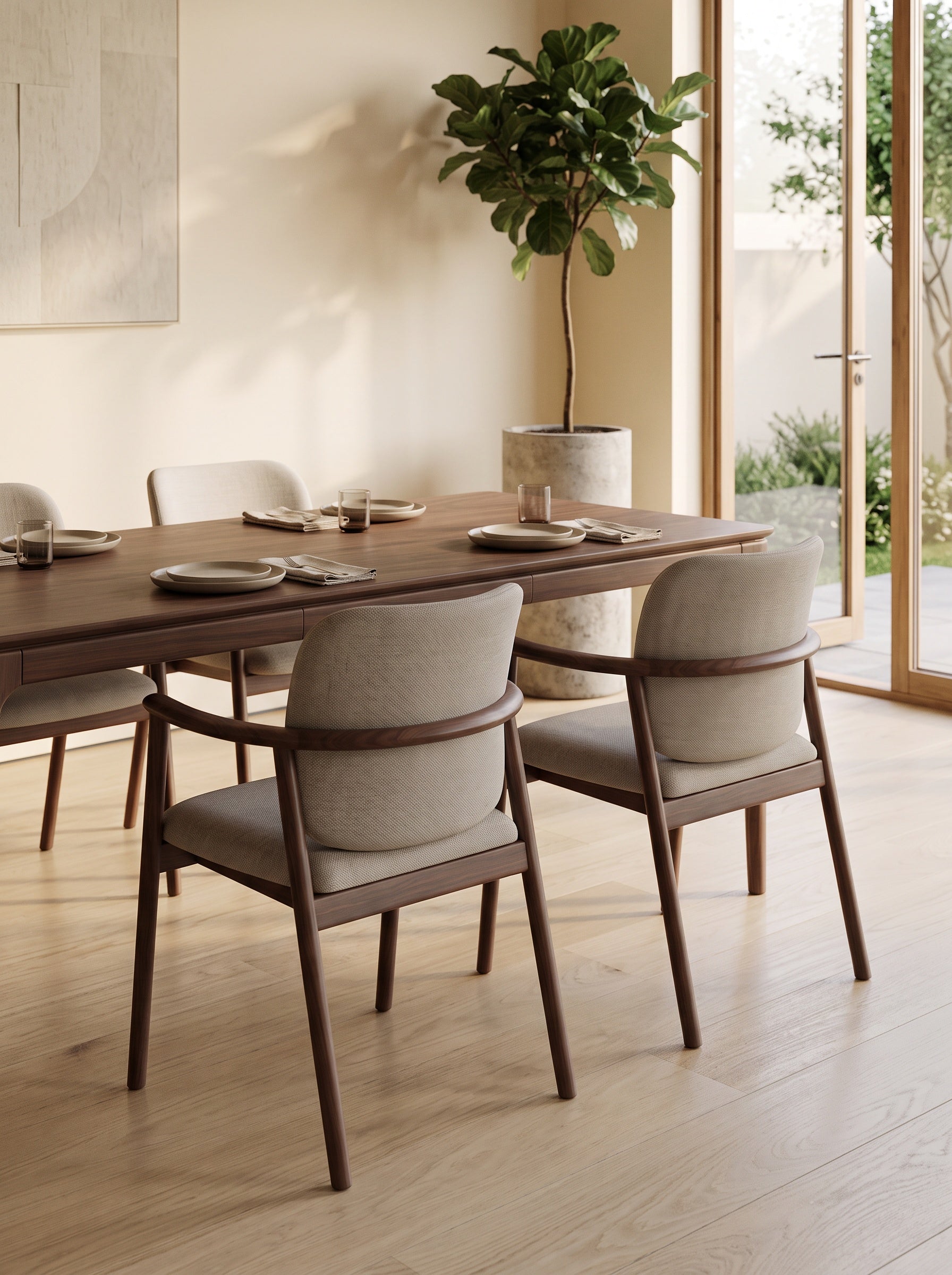 A modern dining table and four upholstered chairs in a warm, sunlit dining room with light wood floors and a potted plant in the background.