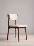 A mid-century modern dining chair with a warm brown wooden frame and cream-colored upholstered seat and backrest, set against a minimalist light gray studio background.