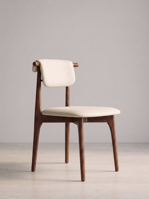 A mid-century modern dining chair with a warm brown wooden frame and cream-colored upholstered seat and backrest, set against a minimalist light gray studio background.